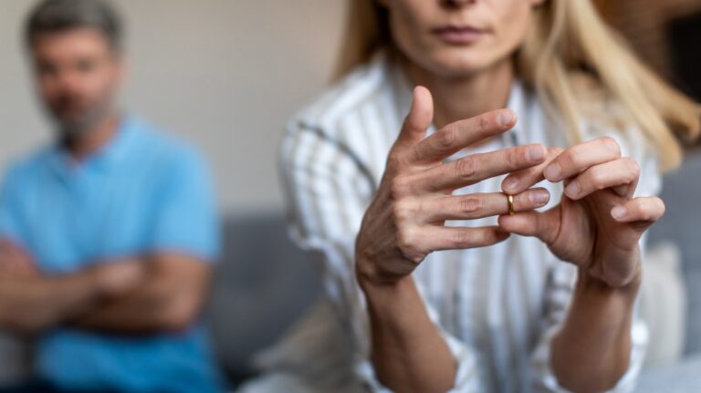 Woman taking of wedding ring with husband in background