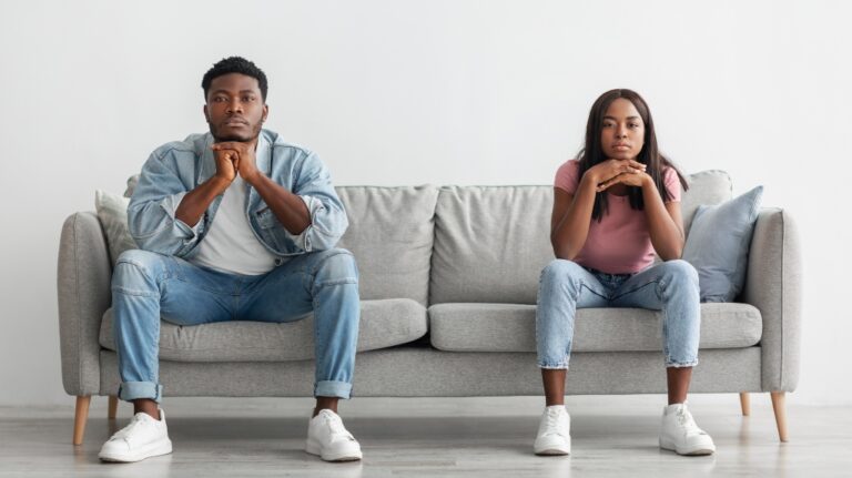 serious young couple sitting separate on the couch at home