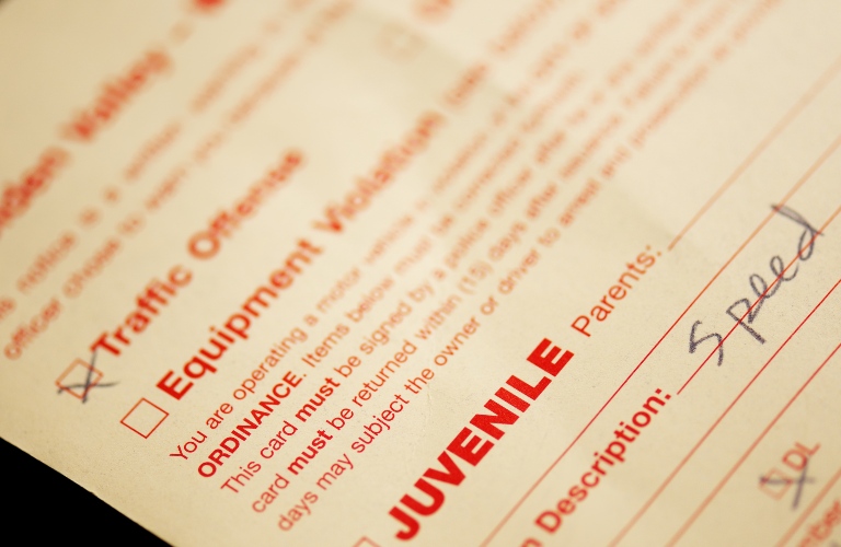 A pale yellow traffic offense ticket, selective focus on the words "juvenile" and "speed"