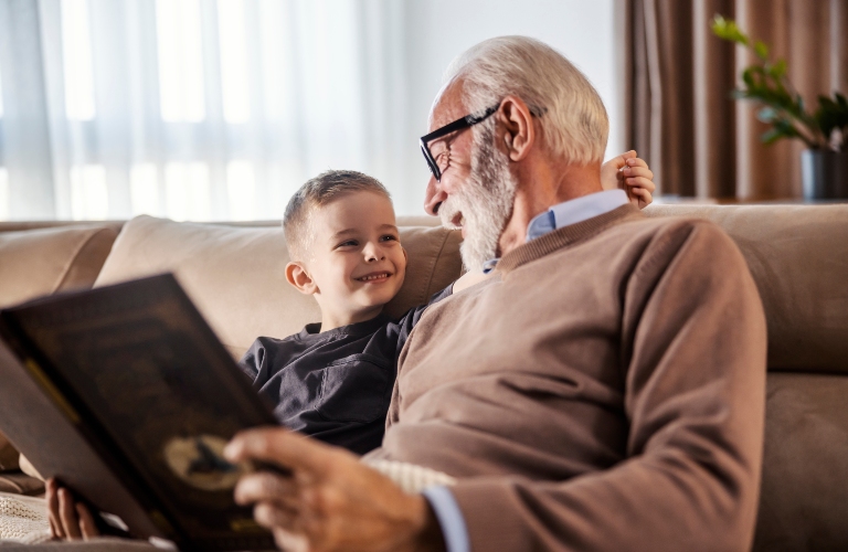 Grandfather is reading a book to his grandchild at home